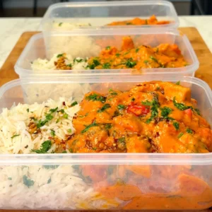 Three meal prep containers filled with creamy Tuscan tofu and rice, garnished with fresh herbs. The tofu is coated in a rich, orange-colored sauce, creating a visually appealing and appetizing dish.