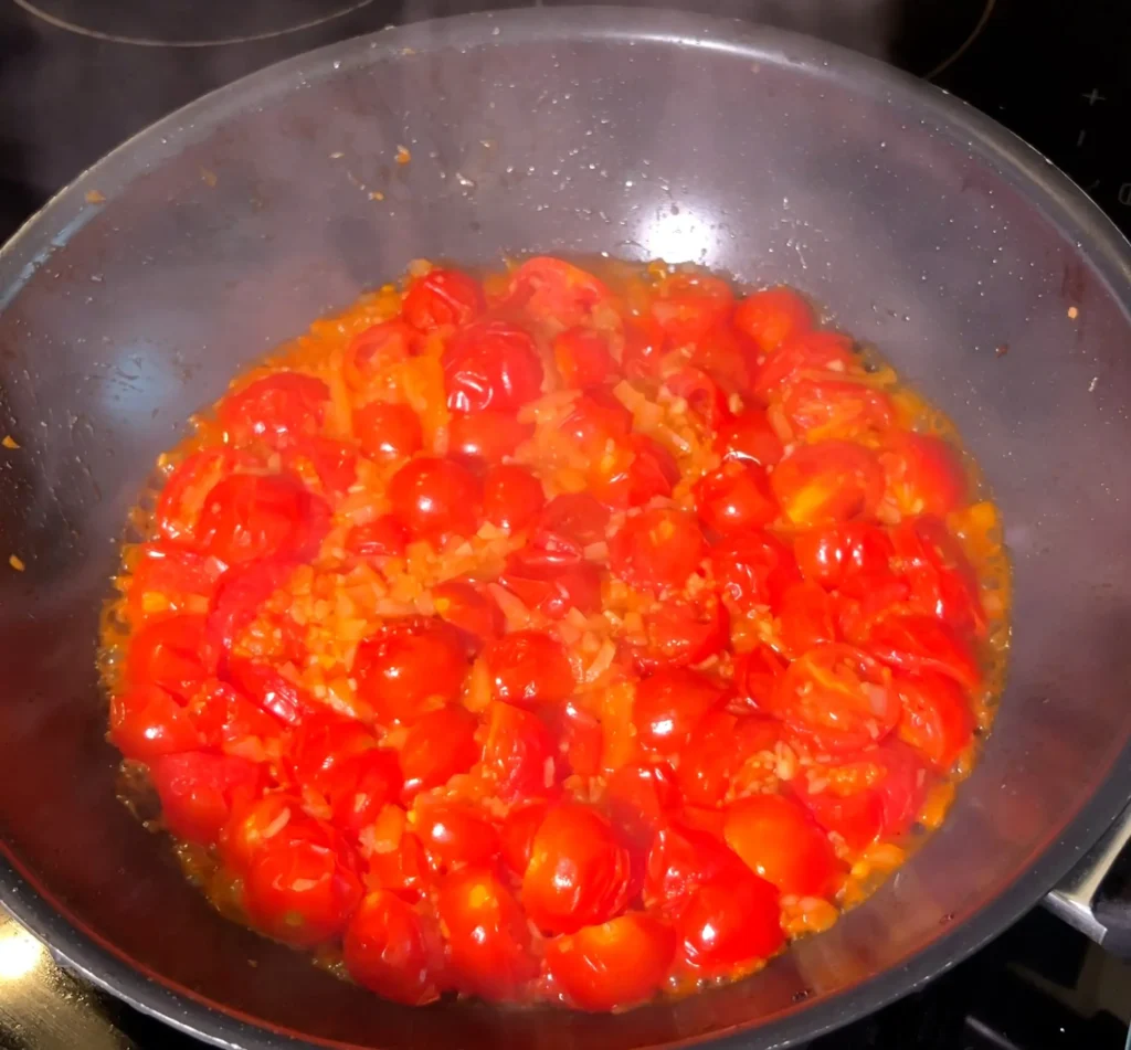 Sautéed cherry tomatoes, onions, and garlic in a pan.