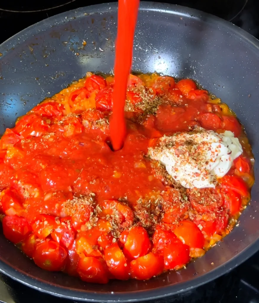 Tomato puree and cream cheese being added to the pan with sautéed vegetables.