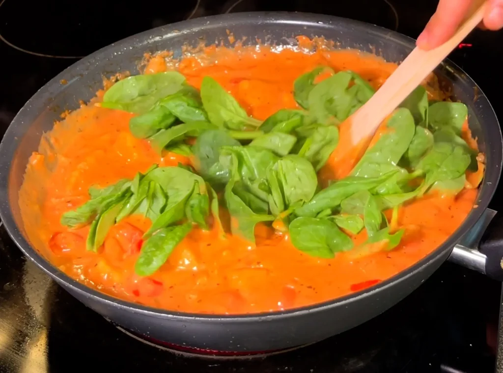 Fresh spinach leaves being stirred into the creamy tofu tomato sauce.