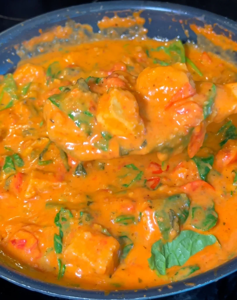 Creamy Tuscan Tofu cooking in a pan with a rich tomato sauce and fresh spinach.