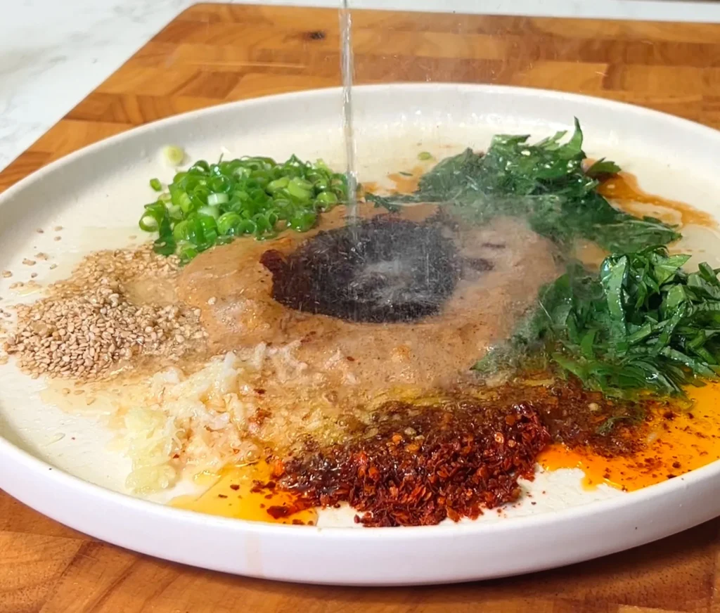 Plate with fresh ingredients like green onions, garlic, chili flakes, and sesame seeds for a spicy noodle sauce.