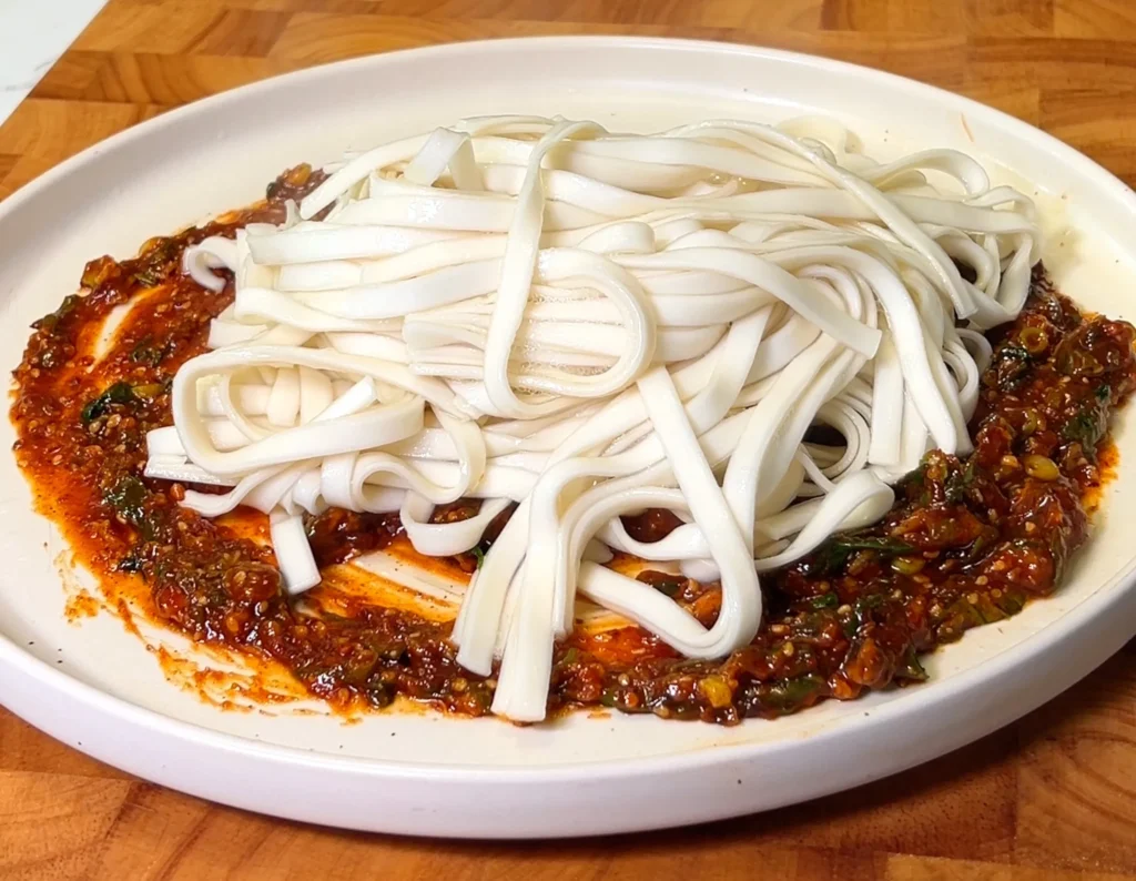 Spicy sesame noodles topped with fresh scallions and sesame seeds on a white plate.