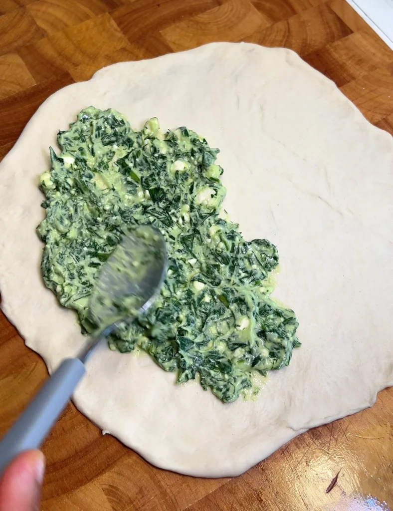 Spreading spinach and cheese filling on rolled empanada dough