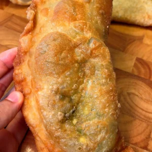 Close-up of a golden fried empanada held in hand