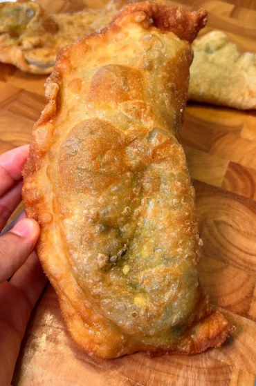 Close-up of a golden fried empanada held in hand