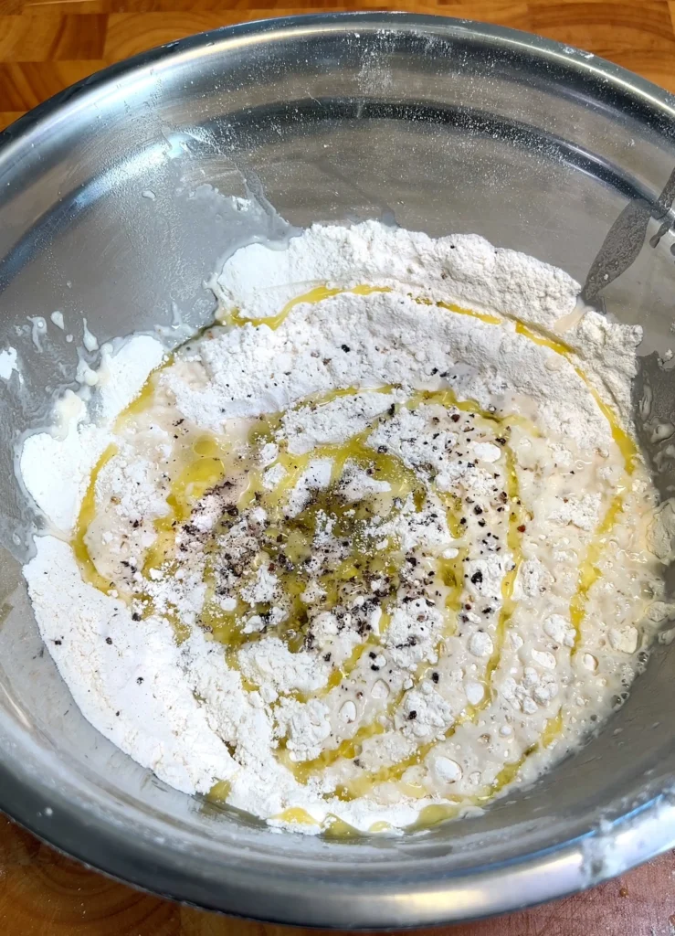 Flour, olive oil, and cracked black pepper in a metal bowl ready for mixing