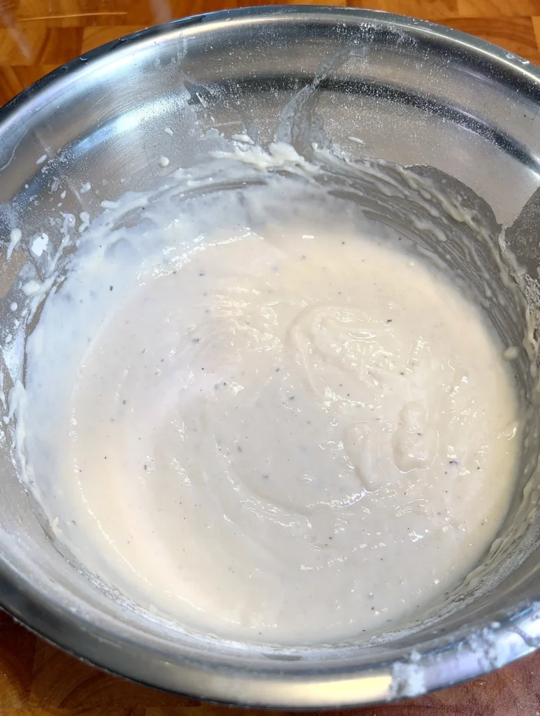 Smooth Schiacciata dough mixture in a metal bowl, ready for rising