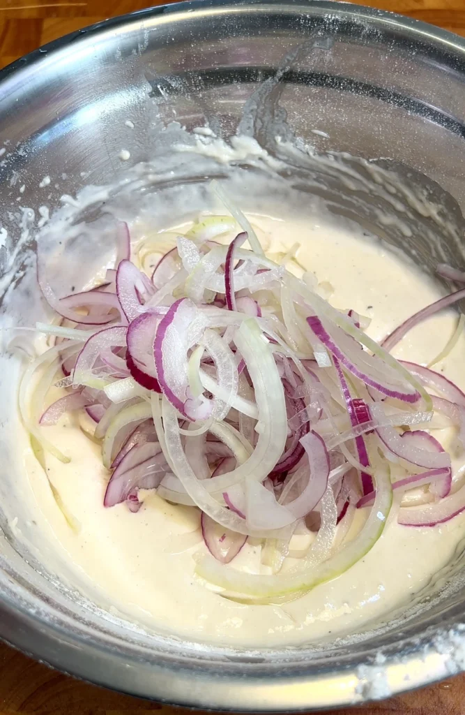 Thinly sliced onions added to Schiacciata dough in a metal bowl