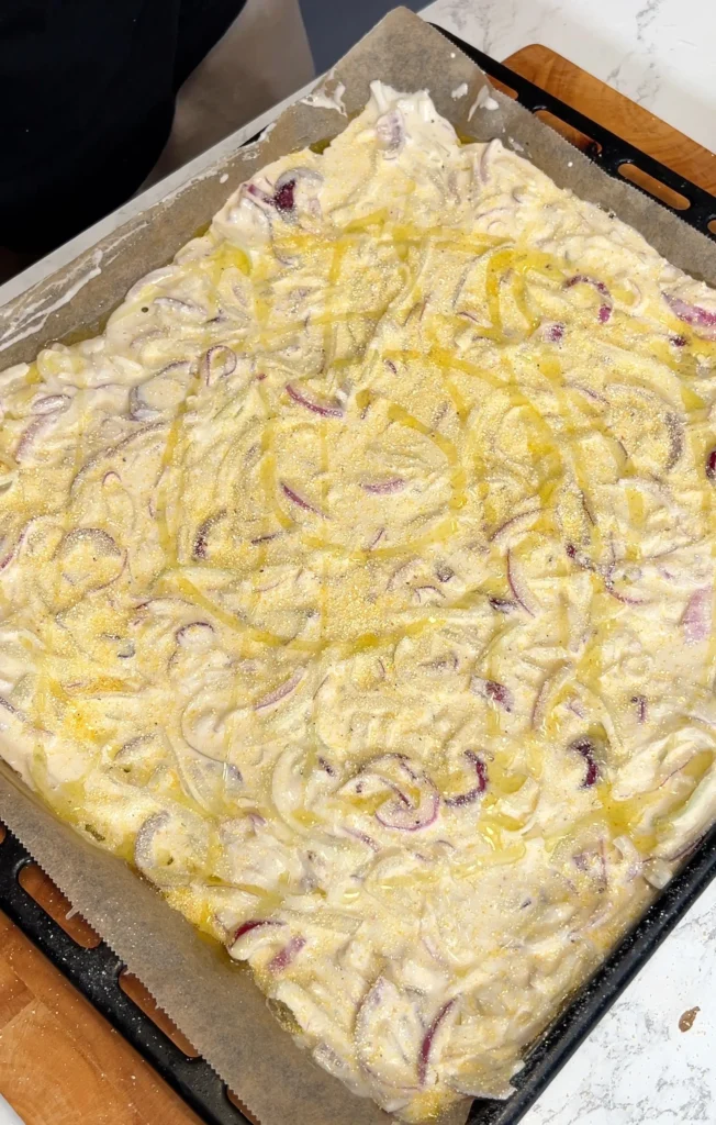 Schiacciata dough topped with onions and drizzled with olive oil on a baking sheet, ready for the oven