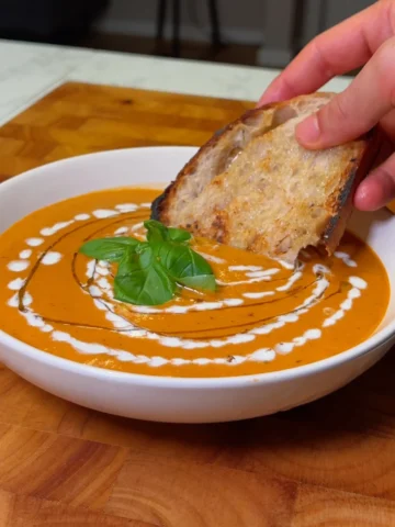 Creamy tomato soup garnished with fresh basil and drizzled with cream, served with a slice of crusty bread.