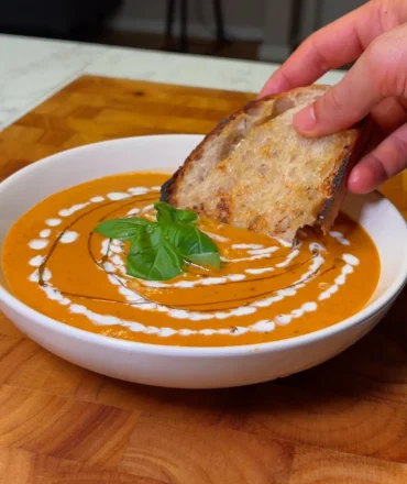 Creamy tomato soup garnished with fresh basil and drizzled with cream, served with a slice of crusty bread.