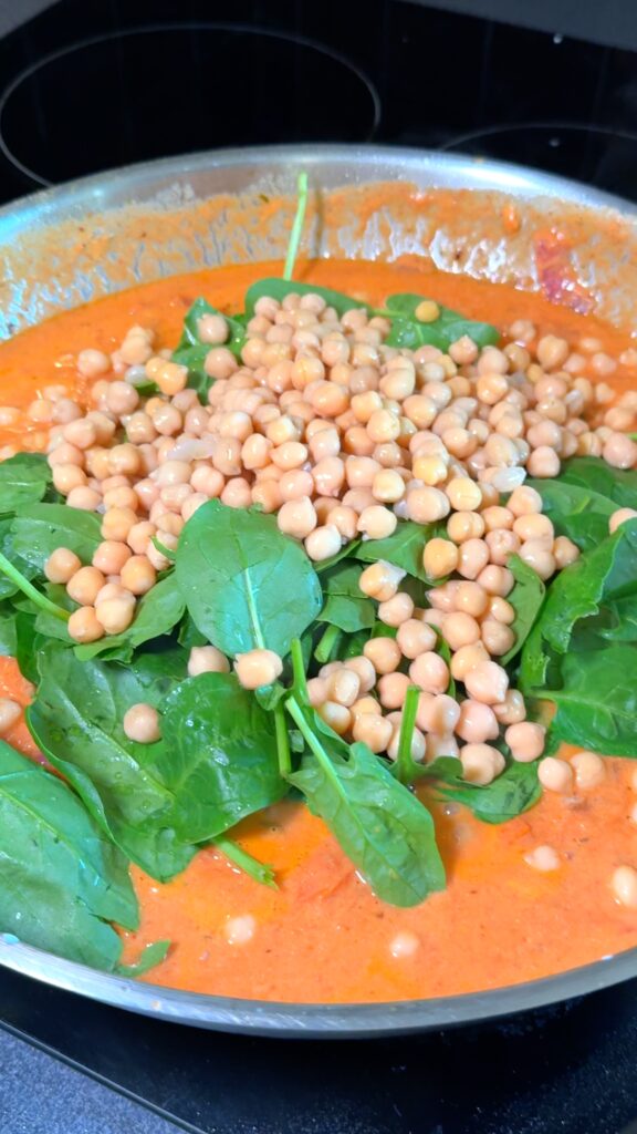 Mixing spinach and chickpeas until spinach wilts.