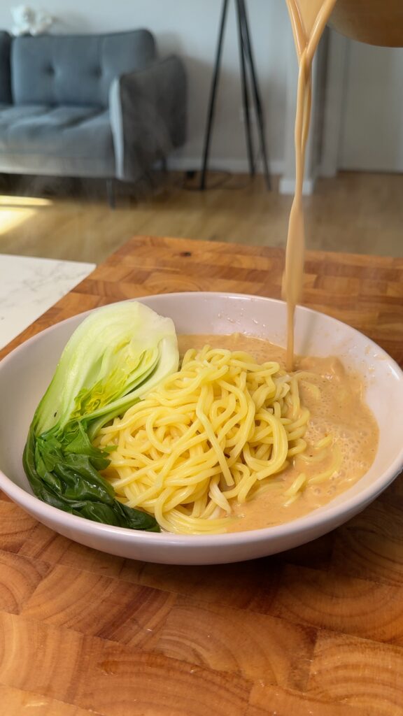 bok choy, noodles and soup being poured in a bowl