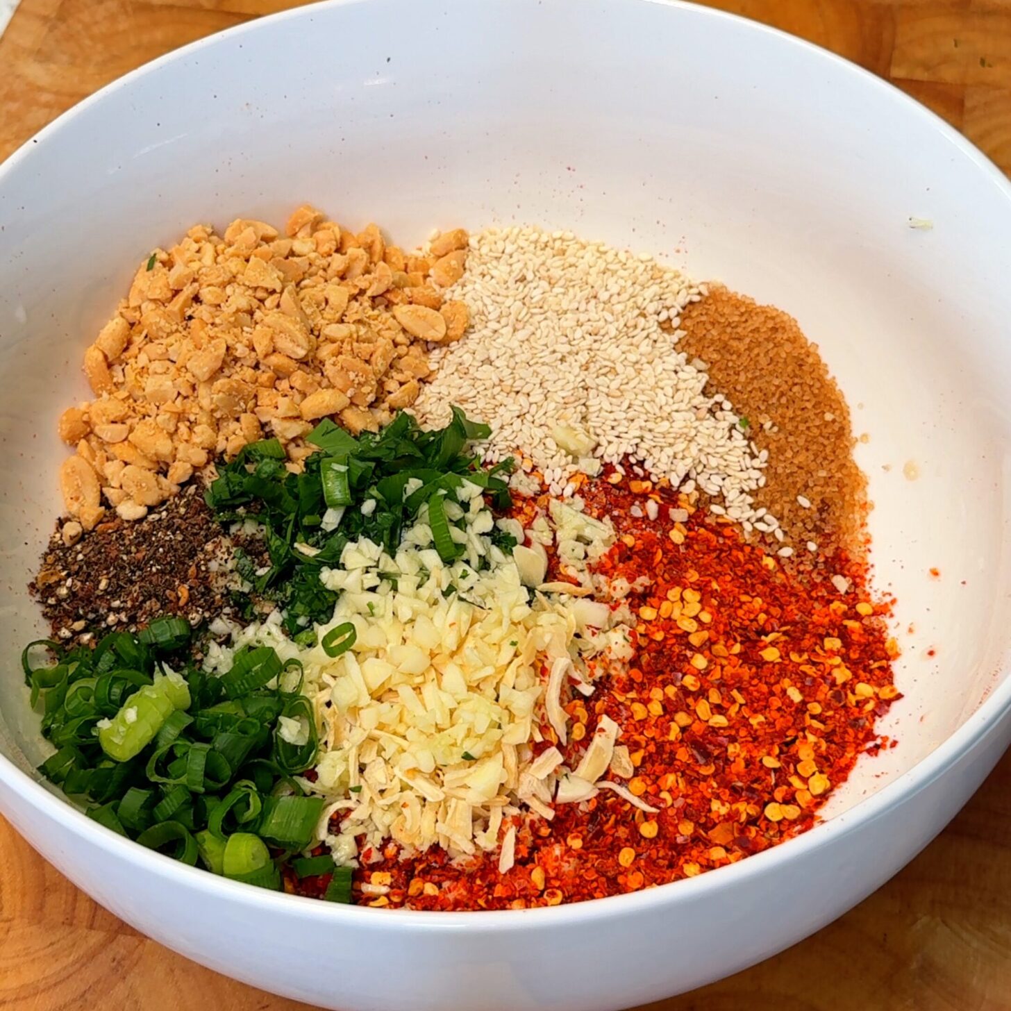 In a heat-proof bowl, stir together chili flakes, sesame seeds, Sichuan peppercorns, garlic, cilantro, spring onion, peanuts, sugar, and salt.