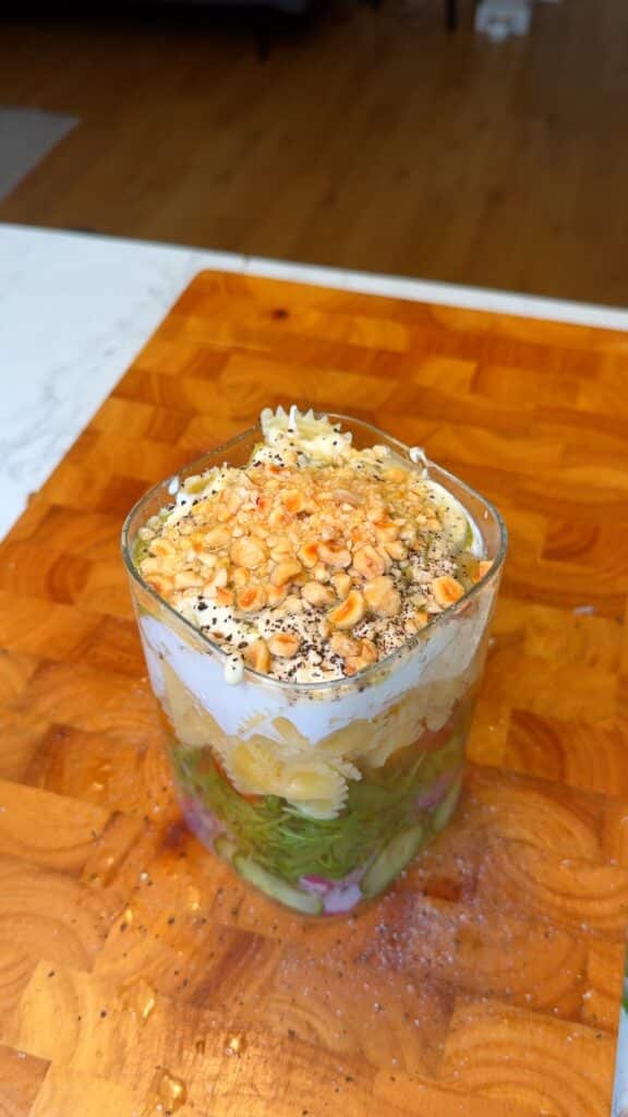 Layer the ingredients. Start with cucumber and build up—onions, arugula, olives, sun-dried and cherry tomatoes, pasta, then the sauces.