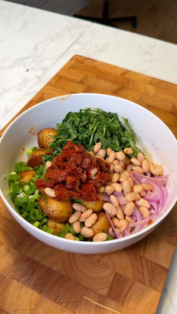 Combine potatoes, onions, arugula, beans, and sun-dried tomatoes in a bowl