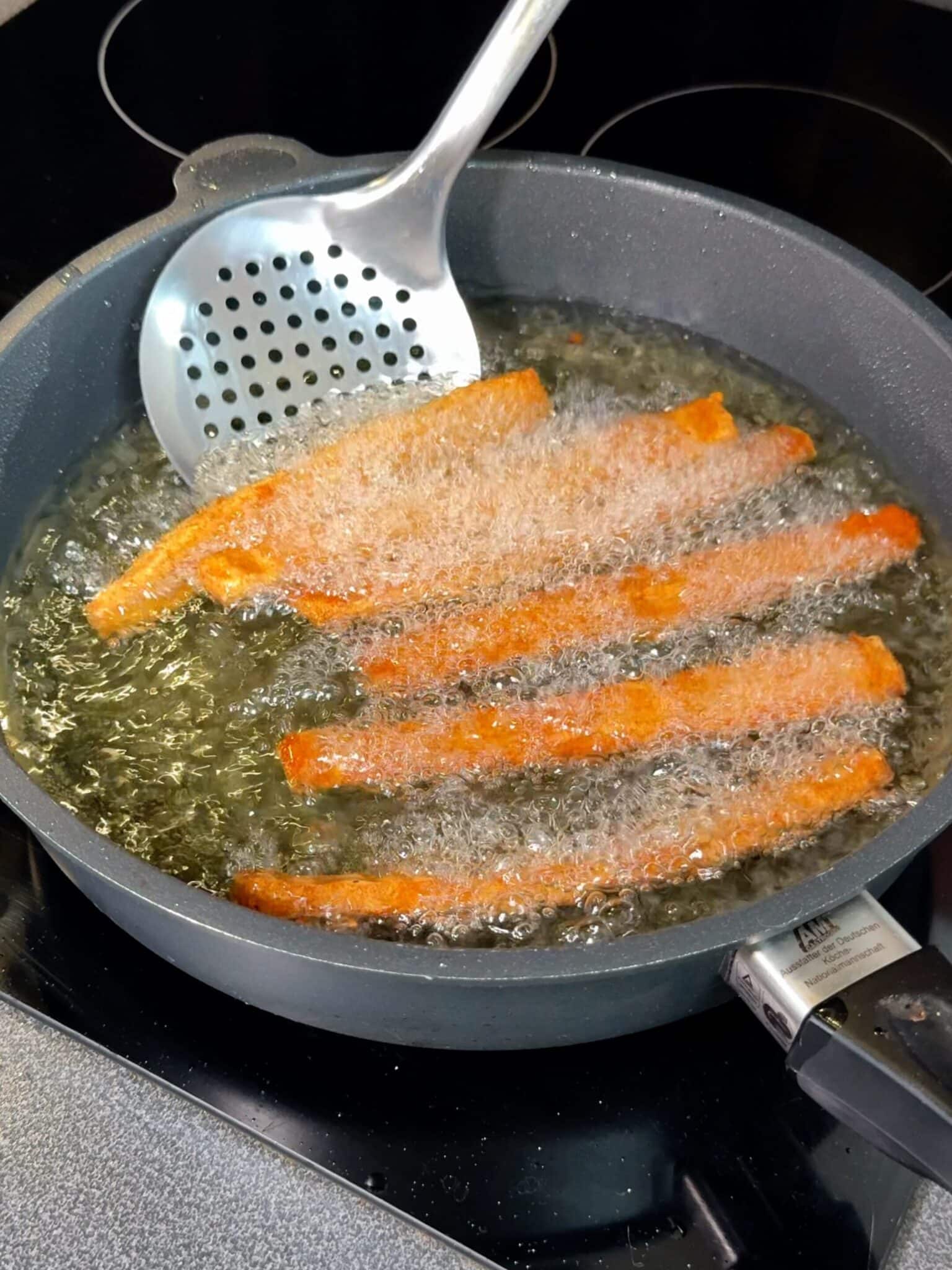 Golden brown fries frying in oil in a deep pan until crispy