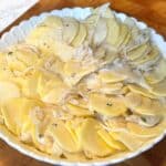 Thinly sliced potatoes coated in cream sauce in a scalloped potato baking dish