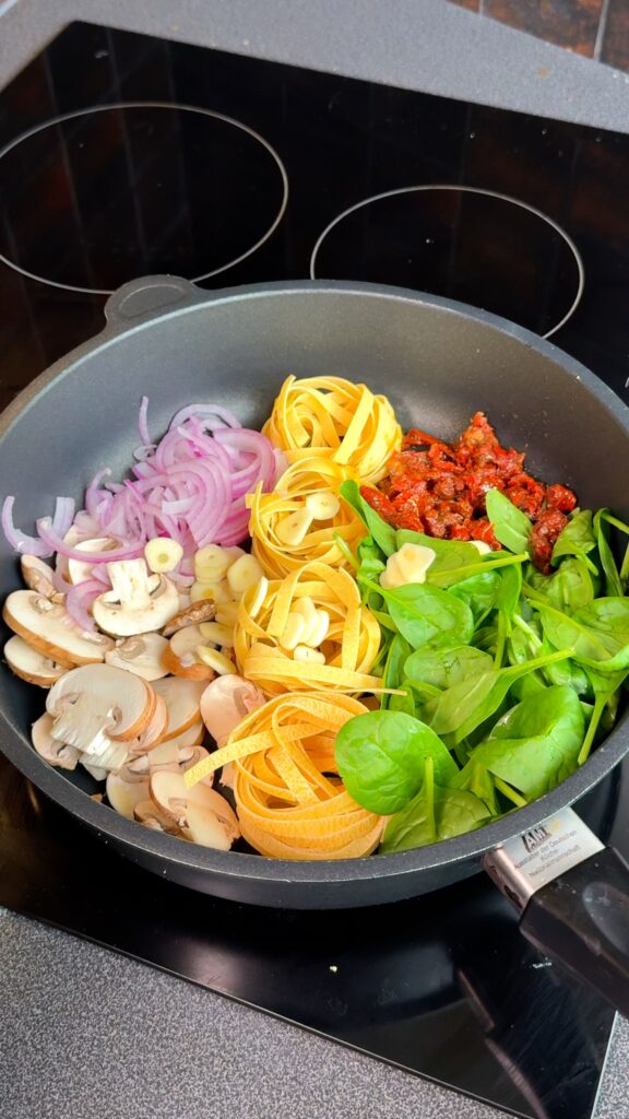 Start by adding your pasta, sliced mushrooms, onion, garlic, spinach, and sun dried tomatoes right into a deep pan.