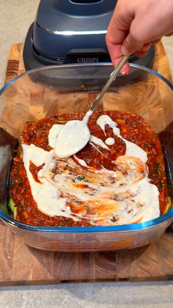 Add more sauce and white sauce
Pour more tomato sauce over the zucchini, then spoon and spread the white sauce lightly.