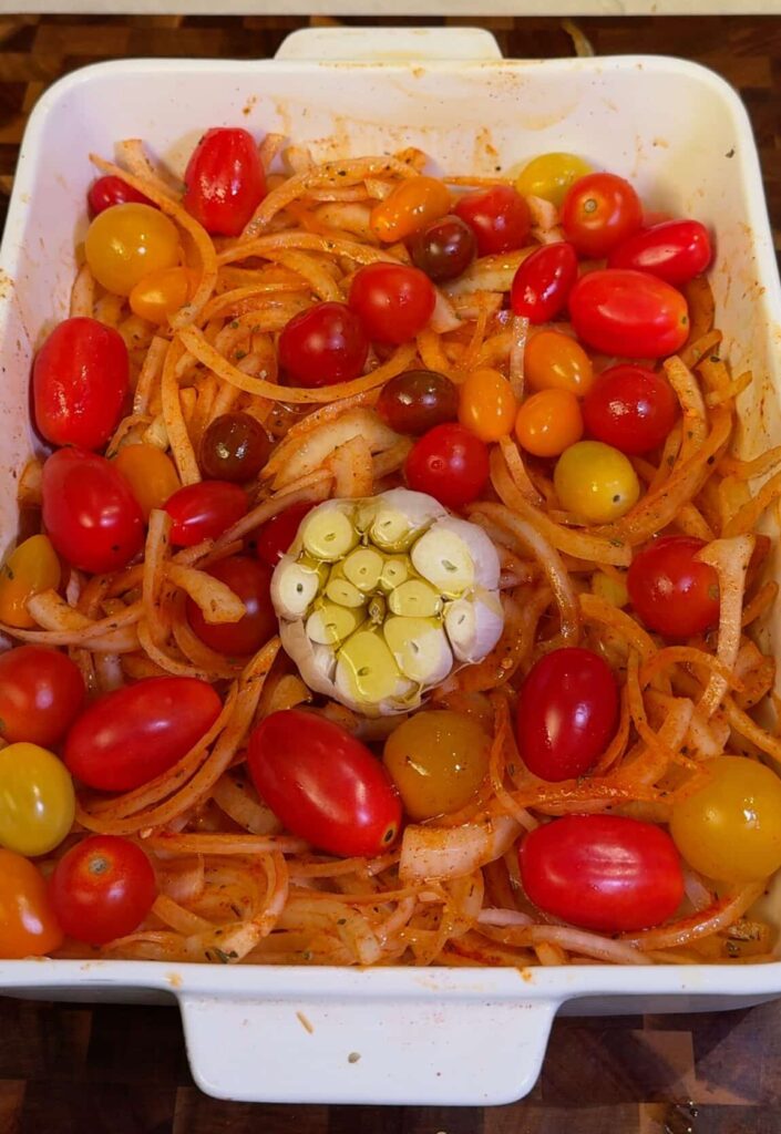Prep the tray and roast Spread seasoned onions and cherry tomatoes on a baking tray with a whole garlic bulb in the center. Cover with foil and roast at 400°F for 40 to 45 minutes.