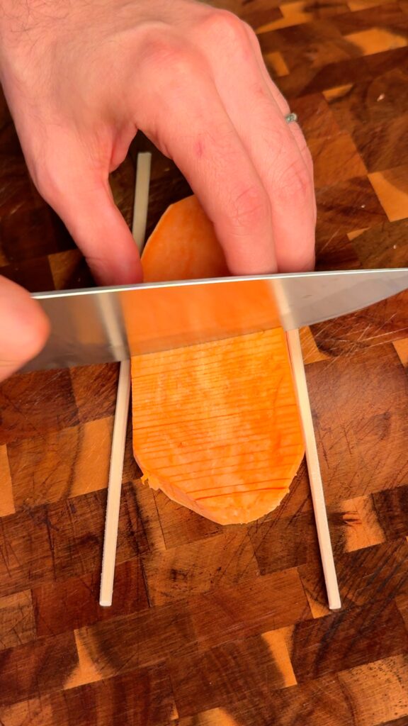 Make the accordion cuts
Place each sweet potato plank between two chopsticks and slice straight across without cutting through. Flip and slice at a 45° angle for the crisscross pattern. Soak in cold water.
