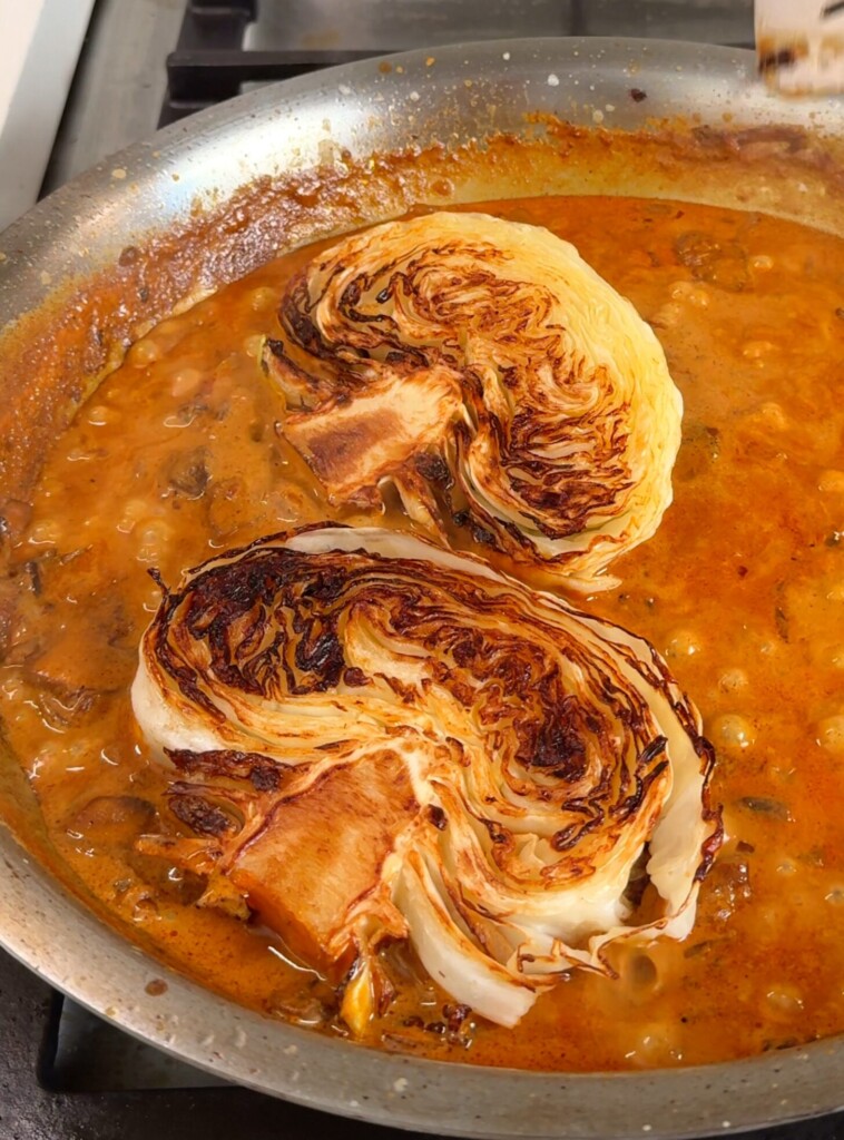 Build the sauce and braise Pour in oat cream and water. Add seasoning, chili crisp, and vegan parmesan. Nestle the seared cabbage back in, spoon sauce over the top, cover, and braise until tender.