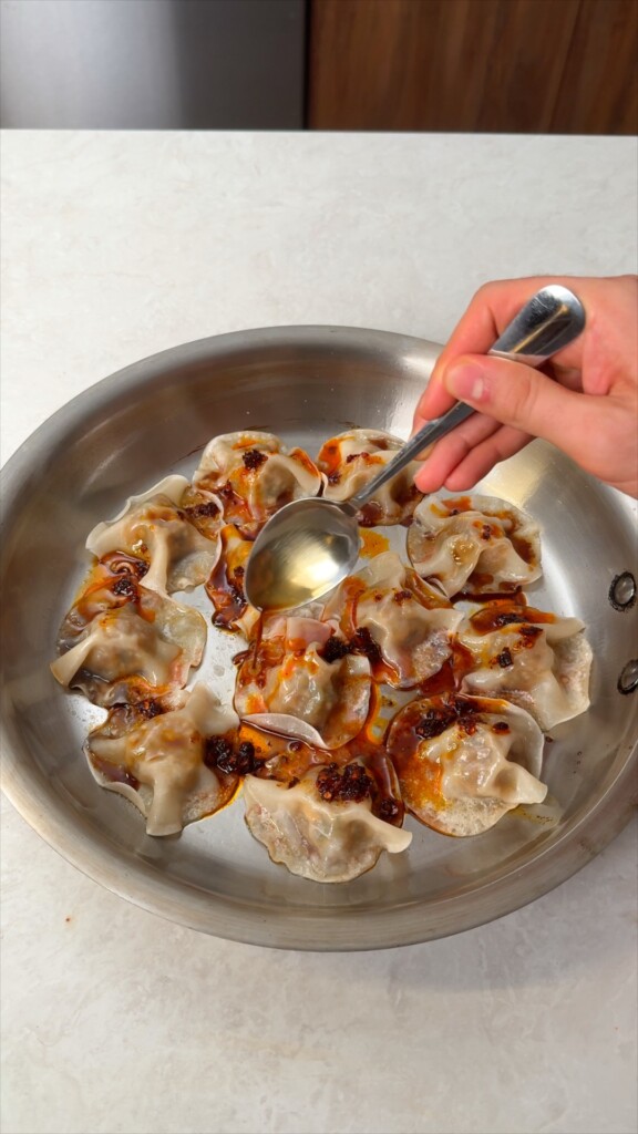 Drizzle and serveSpoon chili crisp and soy sauce generously over the dumplings. The sauce pools around them and soaks into every bite. Finish with sesame seeds and sliced spring onions.