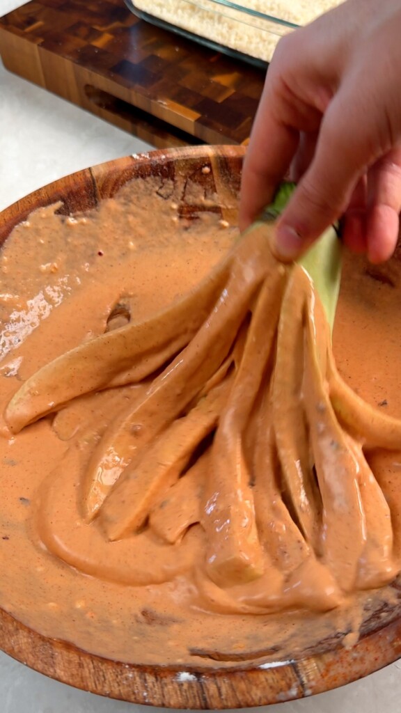 Dip in the batter Grab the eggplant strips by the stem and dip them through the batter, coating every side. Let the excess drip off.
