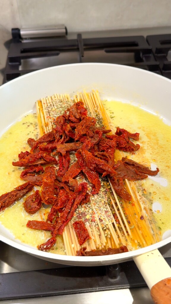 Build the base Melt vegan butter in a large pan. Lay the spaghetti flat, sprinkle with Italian seasoning, and scatter chopped sun-dried tomatoes on top.