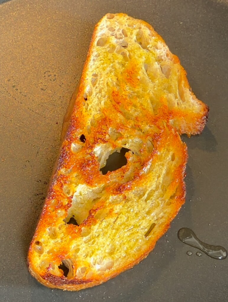 Golden toasted sourdough bread slice in a black pan for pan con tomate recipe