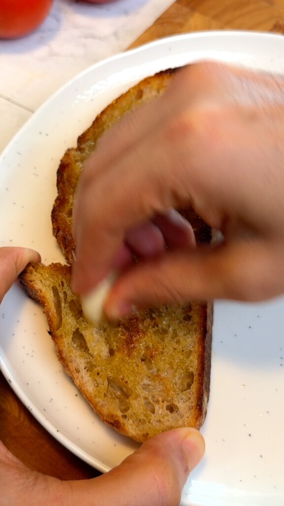 Hand rubbing a raw peeled garlic clove on warm toasted sourdough bread for pa amb tomàquet
