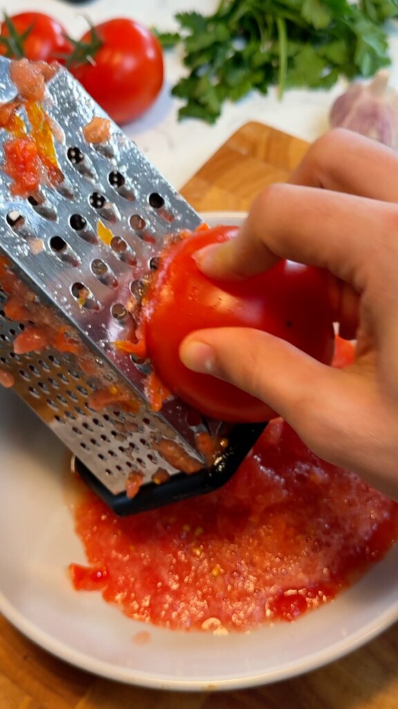 Hand grating a fresh red tomato on a box grater for authentic pan con tomate