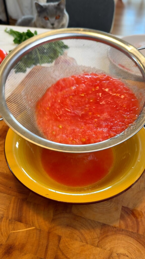 Straining grated tomato pulp through a fine mesh sieve into a yellow bowl for pan con tomate