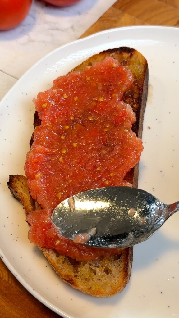 Finished authentic pan con tomate with grated tomato spread over crusty toasted bread on a white plate