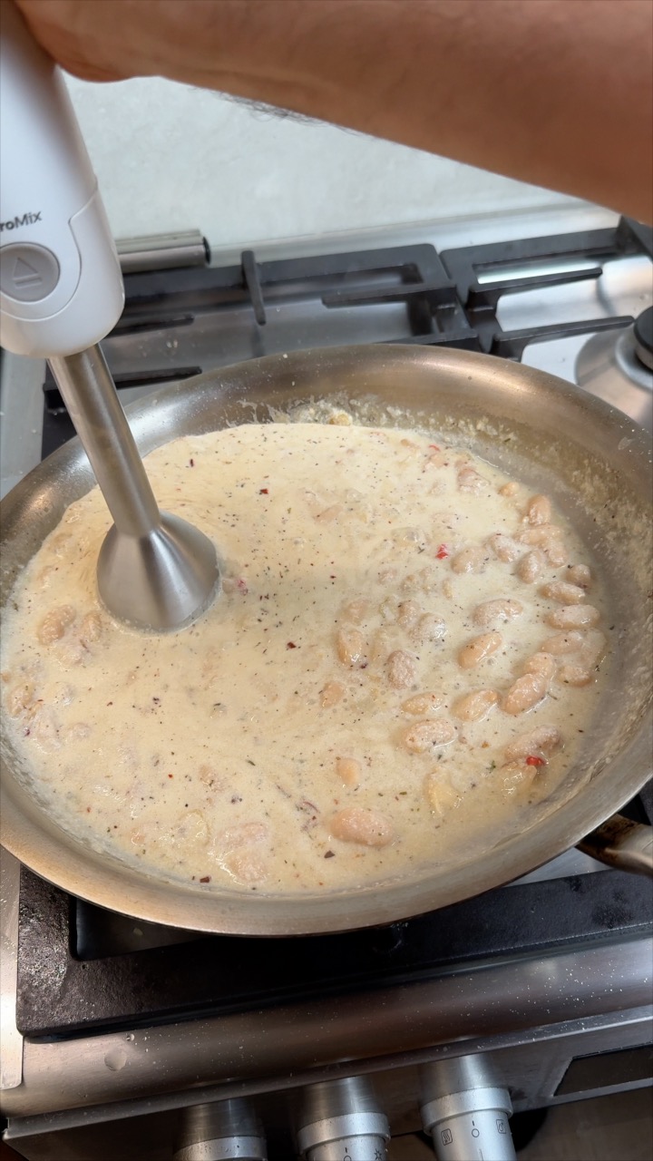 An immersion blender smoothing white beans into a creamy pasta sauce