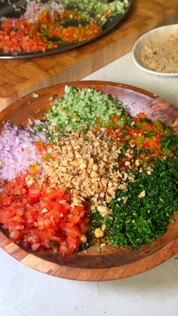 Finely chopped tomato, cucumber, onion, bell pepper, walnuts, and parsley arranged in a wooden bowl