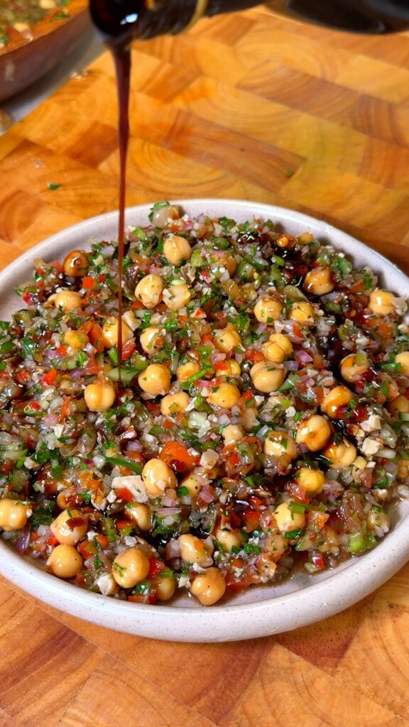 Crispy pita topped with Lebanese balela salad held over a ceramic serving bowl