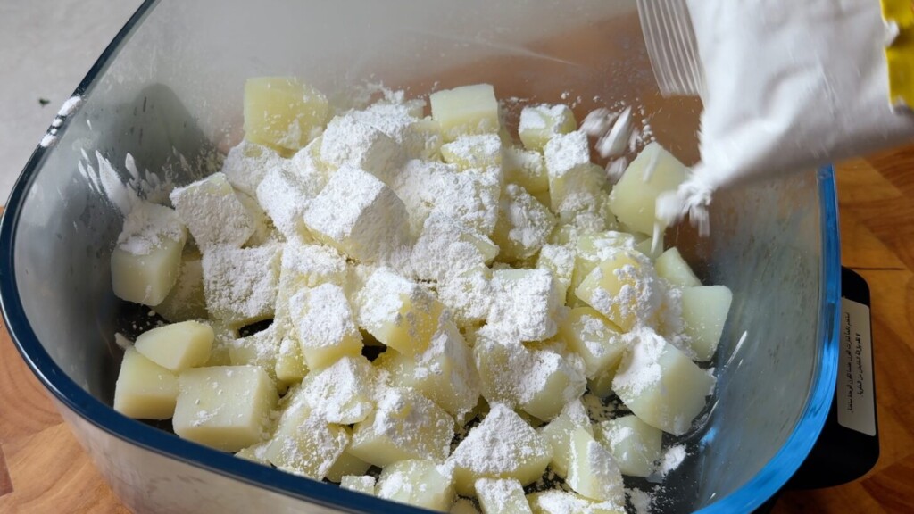 Boiled potato cubes coated in cornstarch in a glass bowl, ready to be pan-fried until crispy