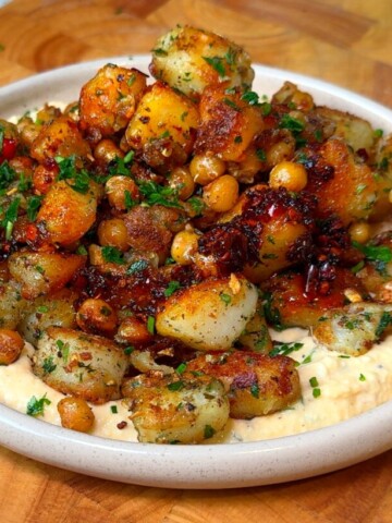 Crispy breakfast potatoes with chickpeas served over hummus, drizzled with chili crisp and parsley