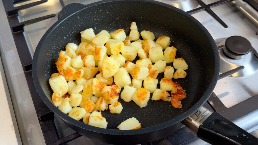 Golden crispy pan-fried potato cubes in a black skillet on a gas stovetop