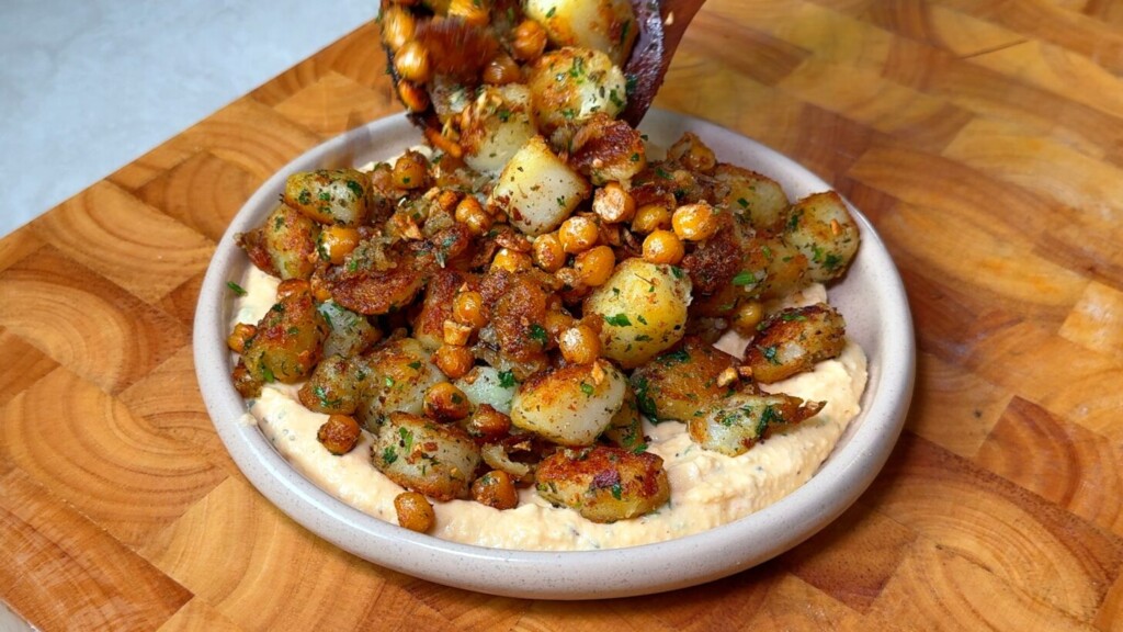 Crispy breakfast potatoes piled over creamy hummus, finished with parsley and a drizzle of chili crisp on a serving plate