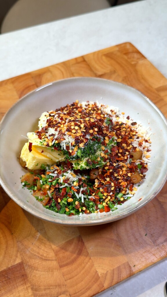 Bowl of roasted garlic with vegan butter, vegan parmesan, parsley, and chili flakes for garlic butter eggplant spread