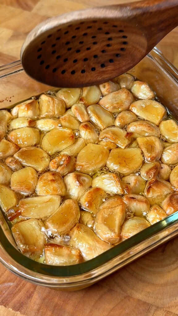 Whole roasted garlic cloves in olive oil in a glass baking dish for vegan roasted garlic eggplant