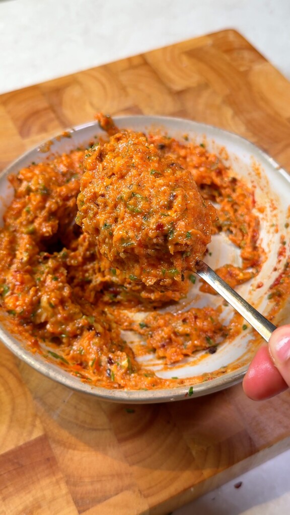 Creamy roasted garlic butter spread on a spoon, with vegan parmesan, herbs, and chili flakes for stuffed eggplant