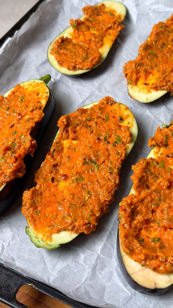 Halved eggplants topped with roasted garlic butter spread on a parchment-lined baking tray ready for the oven