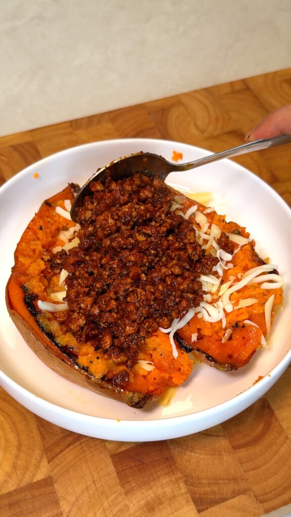 Smoky tofu beef crumble being spooned over cheesy stuffed sweet potatoes