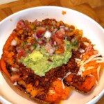 Mexican stuffed sweet potatoes topped with guacamole, charred corn, and fresh tomato-onion salsa in a white bowl