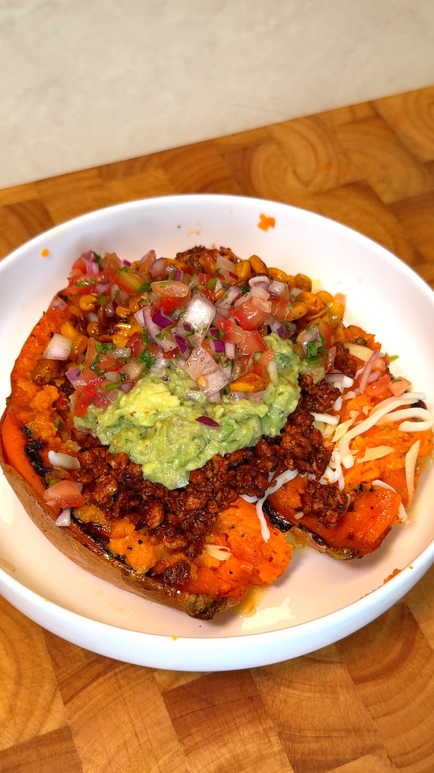 Mexican stuffed sweet potatoes topped with guacamole, charred corn, and fresh tomato-onion salsa in a white bowl